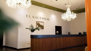 A reception area with a wooden reception desk, two chandeliers, and a wall-mounted sign that reads "EL NACIONAL". - El Nacional Hotel (Dropull i Poshtëm)