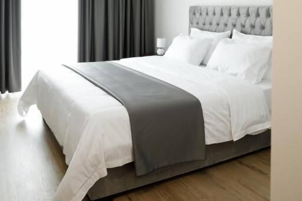A modern bedroom with a large bed, grey curtains, and a white ceiling light.