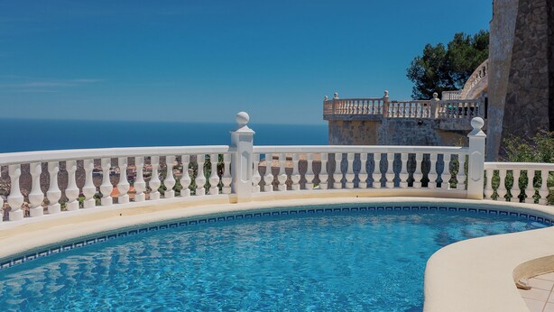A pool with a white balustrade and a view of the sea.