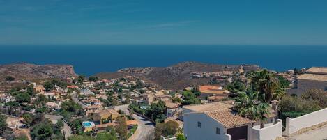Un pueblo costero con casas de tejados de terracota, cielo azul claro y el mar al fondo.