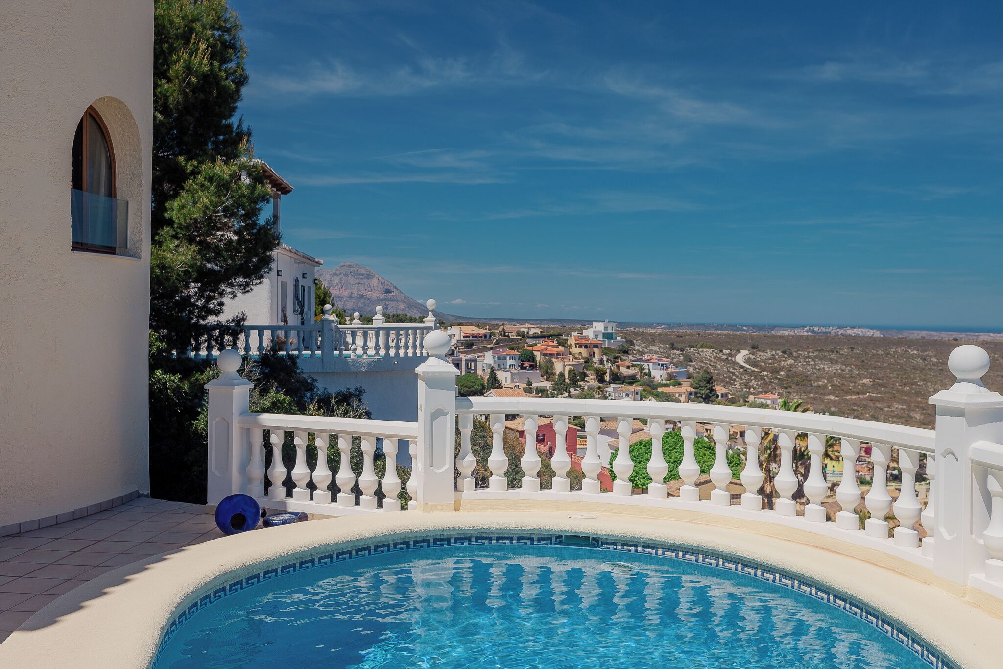 A pool area with a white balustrade, a clear blue sky, and a view of a town in the distance.