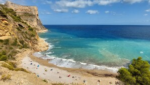 A coastal beach with rocky cliffs, clear turquoise waters, and people enjoying the sun and sea.