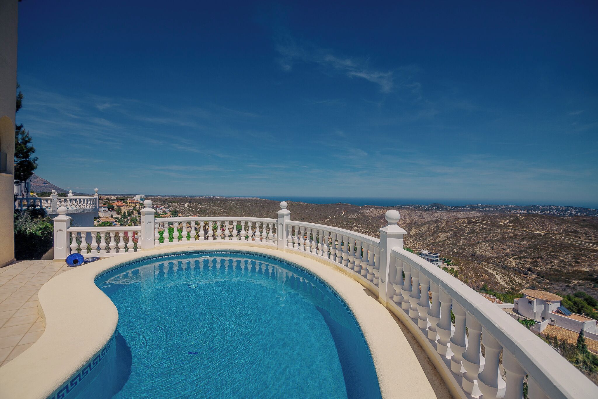 Ein Pool mit weißem Geländer, einem strahlend blauen Himmel und Blick auf eine gebirgige Landschaft.