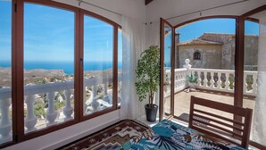 A balcony with a view of the sea, a potted plant, and a wooden bench.