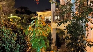 Ein gut beleuchtetes Gebäude mit einem Balkon, umgeben von verschiedenen Pflanzen und Sträuchern.