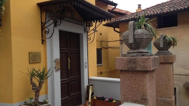 A yellow building with a brown door, a stone pillar, and a small potted plant.
