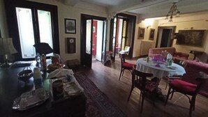 A dining area with a round table, chairs, and a red sofa. There is a window with curtains, a chandelier, and a door leading to another room.