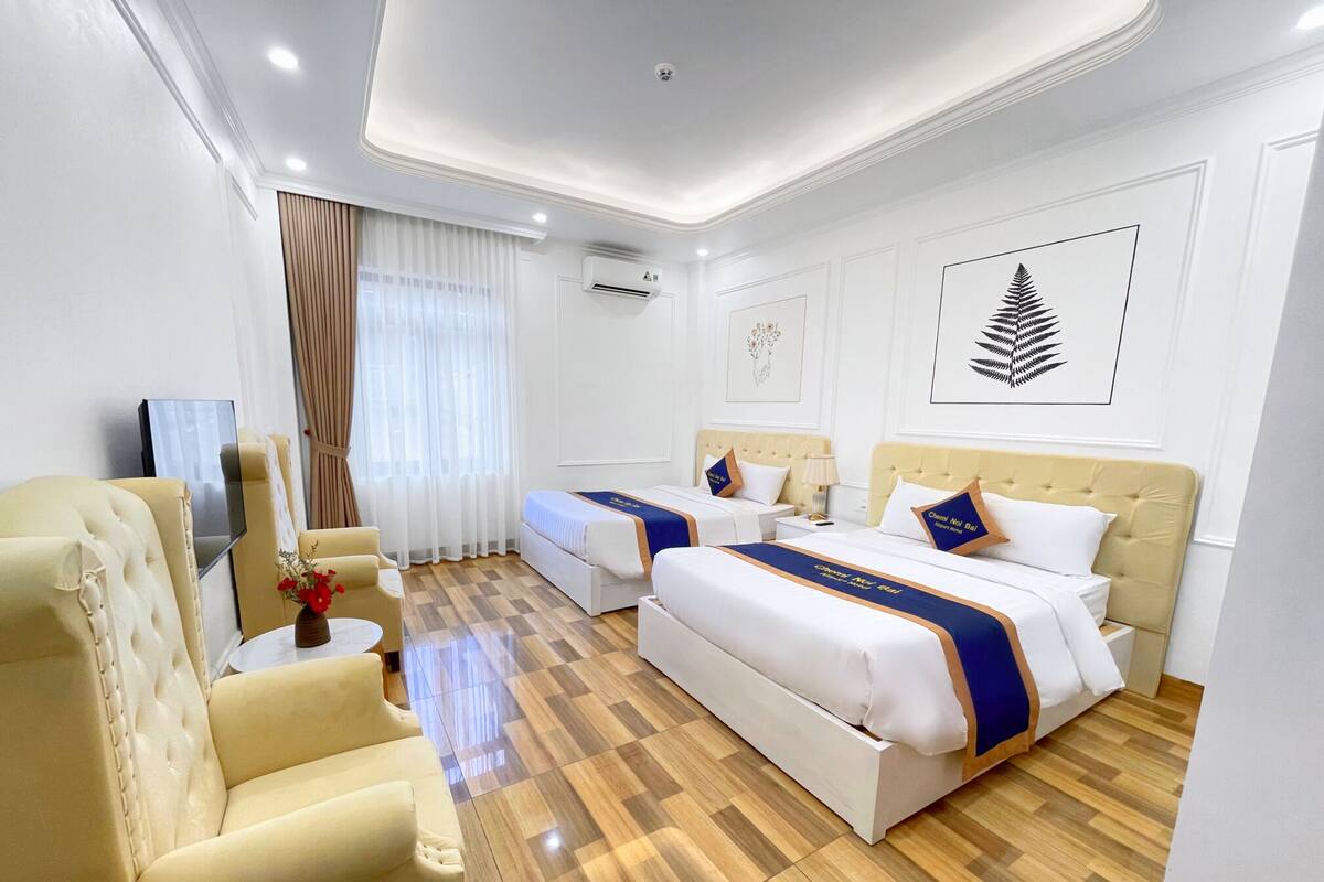 A hotel room with two beds, a TV, a sofa, and a small table with a vase.