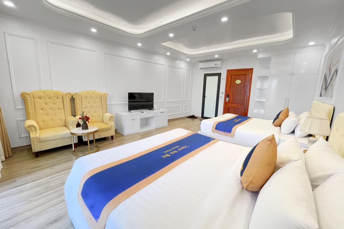 A hotel room with two beds, a sofa, a TV, and a small table with a vase.