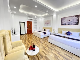 Quarto de hotel com duas camas, um sofá, uma mesinha com garrafa e copos, e piso de madeira.