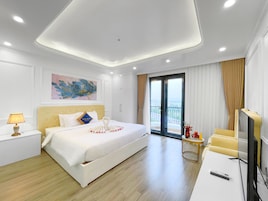 Quarto de hotel com cama, mesa de cabeceira, luminária, obras de arte e varanda com cortinas.