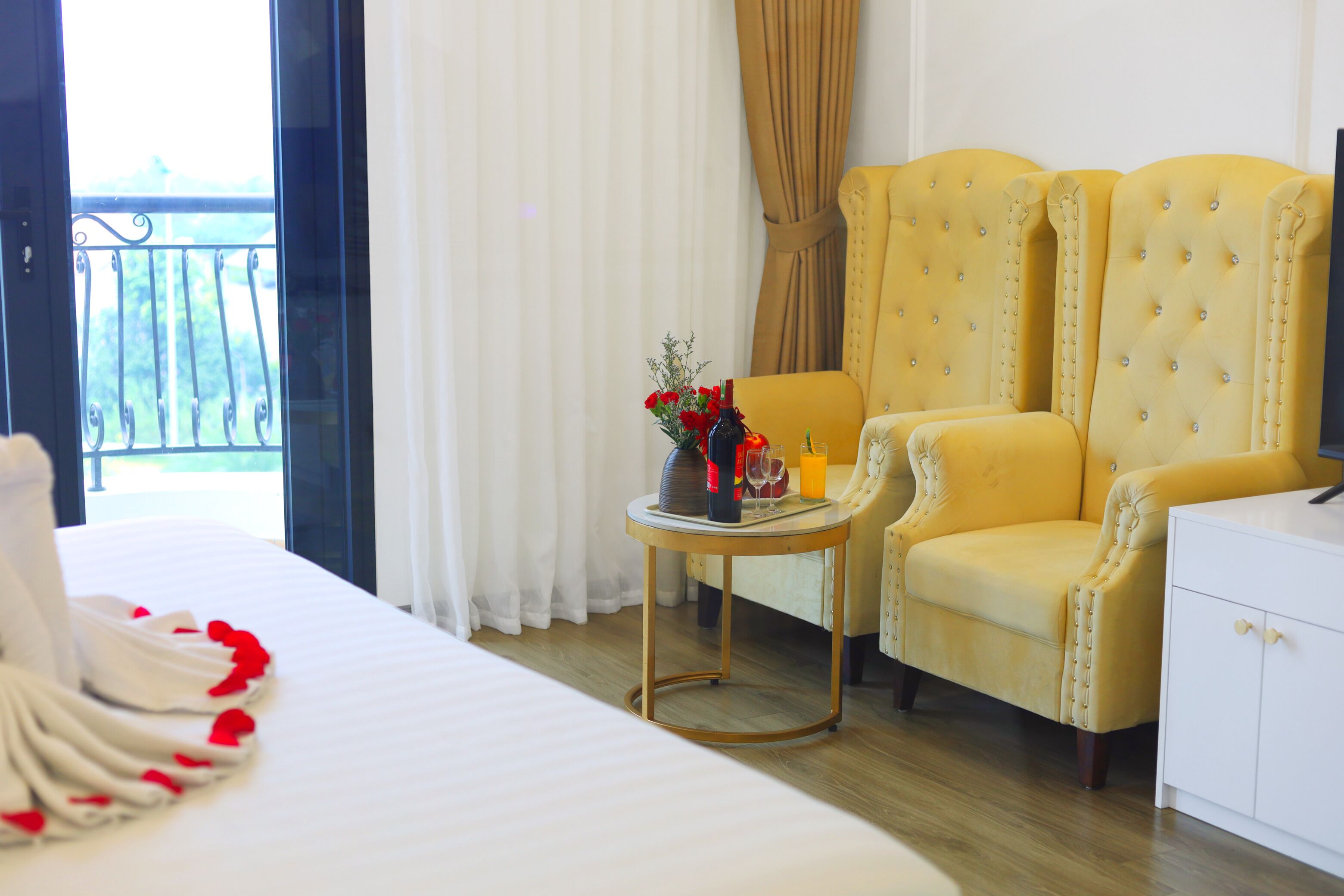 Habitación de hotel con una cama, un sillón amarillo, una mesita con un florero y vistas al exterior.