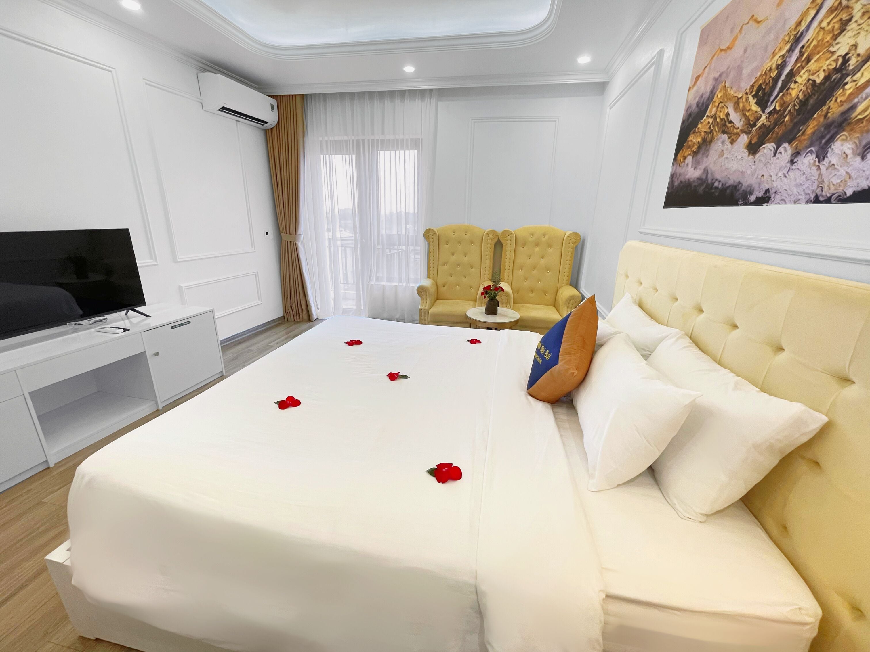 A hotel room with a bed, a TV, a yellow armchair, and a small table with a vase.