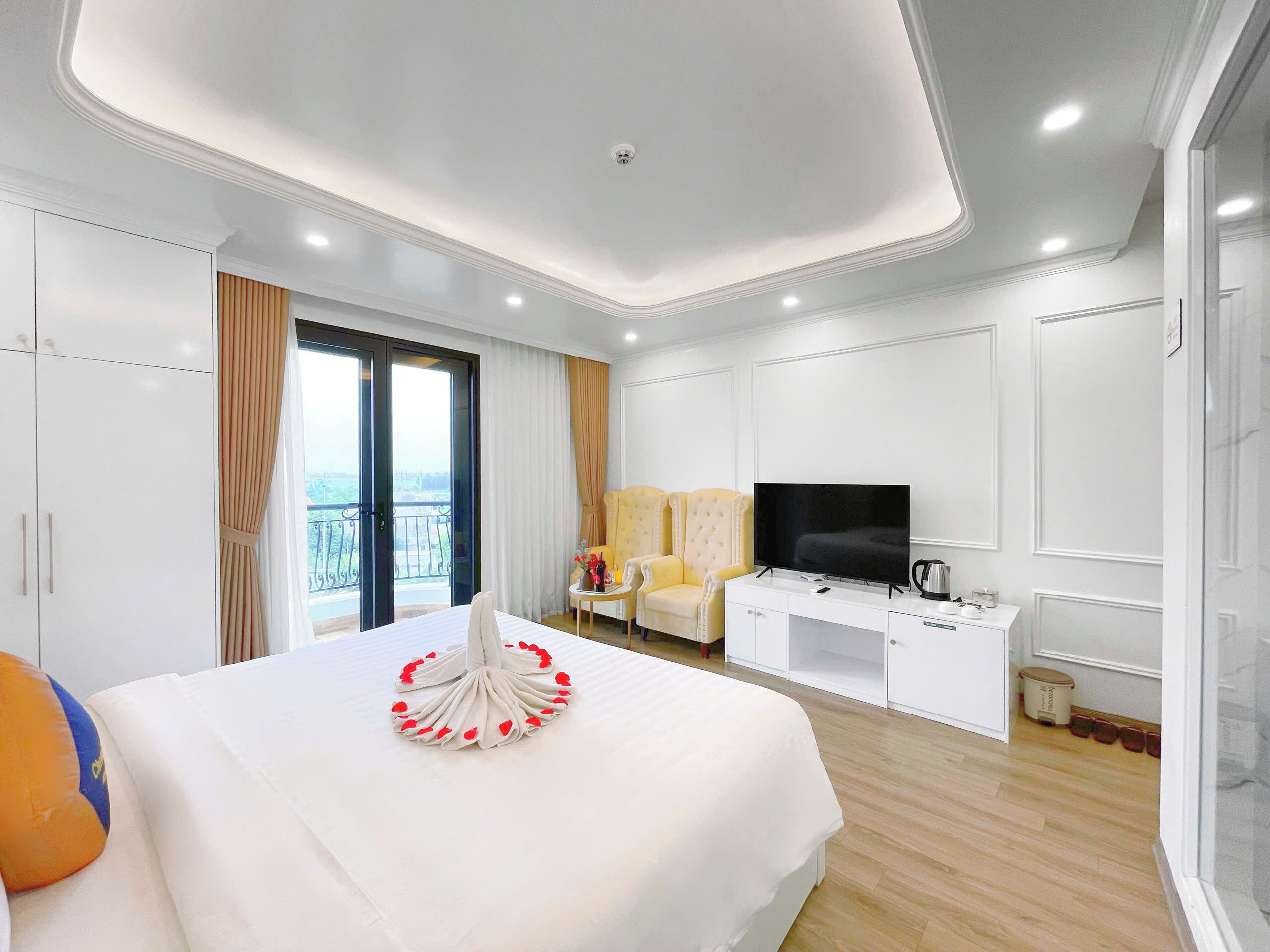 Habitación de hotel con cama, televisor, escritorio y balcón con cortinas.