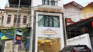 Un hôtel appelé CHEMI HOTEL, reconnaissable à son enseigne bien visible, sa façade moderne et une voiture garée devant.