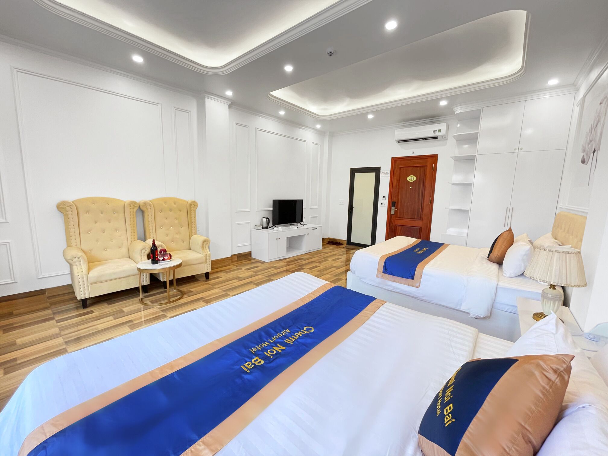 A hotel room with two beds, a sofa, a TV, and a wardrobe.