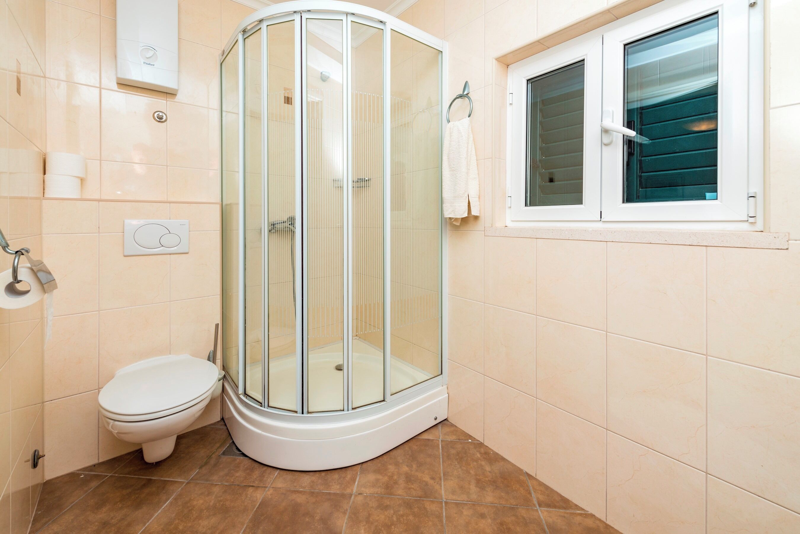 A bathroom with a glass-enclosed shower, a toilet, a towel rack, and a window.