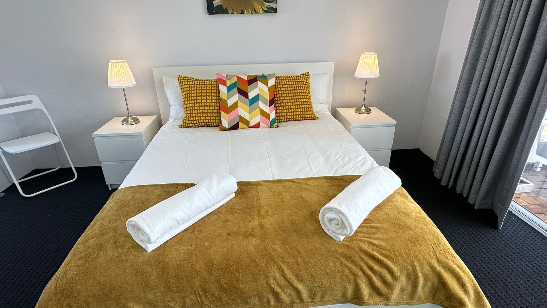 Una habitación de hotel con una cama, dos mesitas de noche, una silla y una ventana con cortinas.