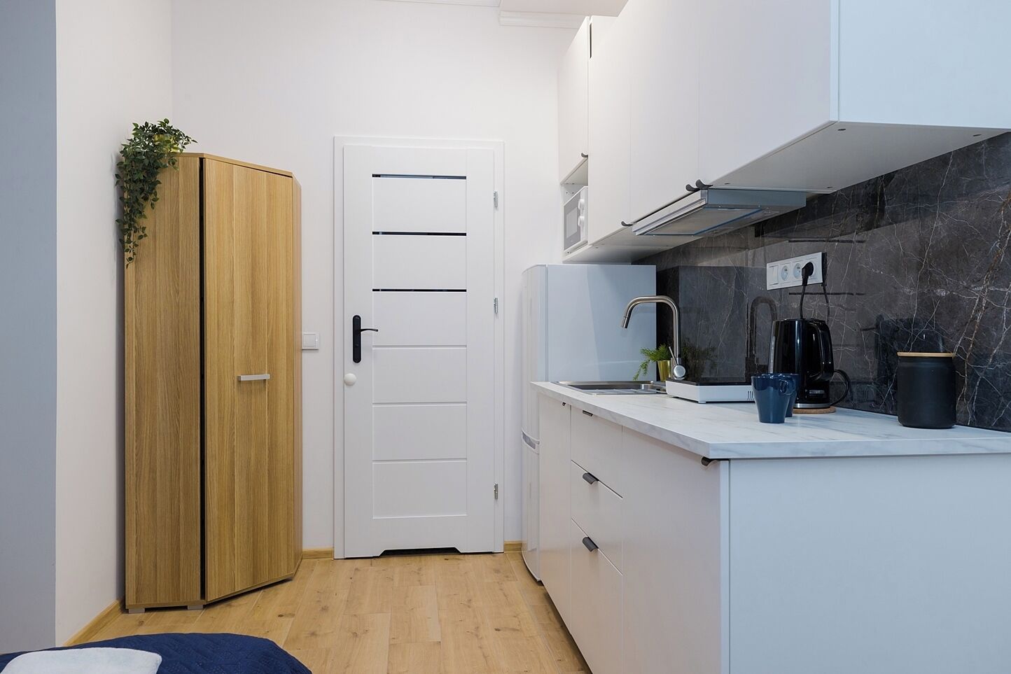 A compact kitchen with a wooden wardrobe, a white door, and a marble backsplash.