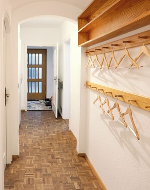A hallway with wooden flooring, a white door, and a wall-mounted wooden rack with clothes hangers.