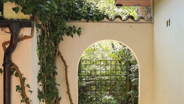 A stone pathway leading through an arched doorway, surrounded by greenery and a metal pipe on the left. - Munich center just a 10-minute subway ride away: 130 m², 4 bedrooms, 2 bathrooms (München)