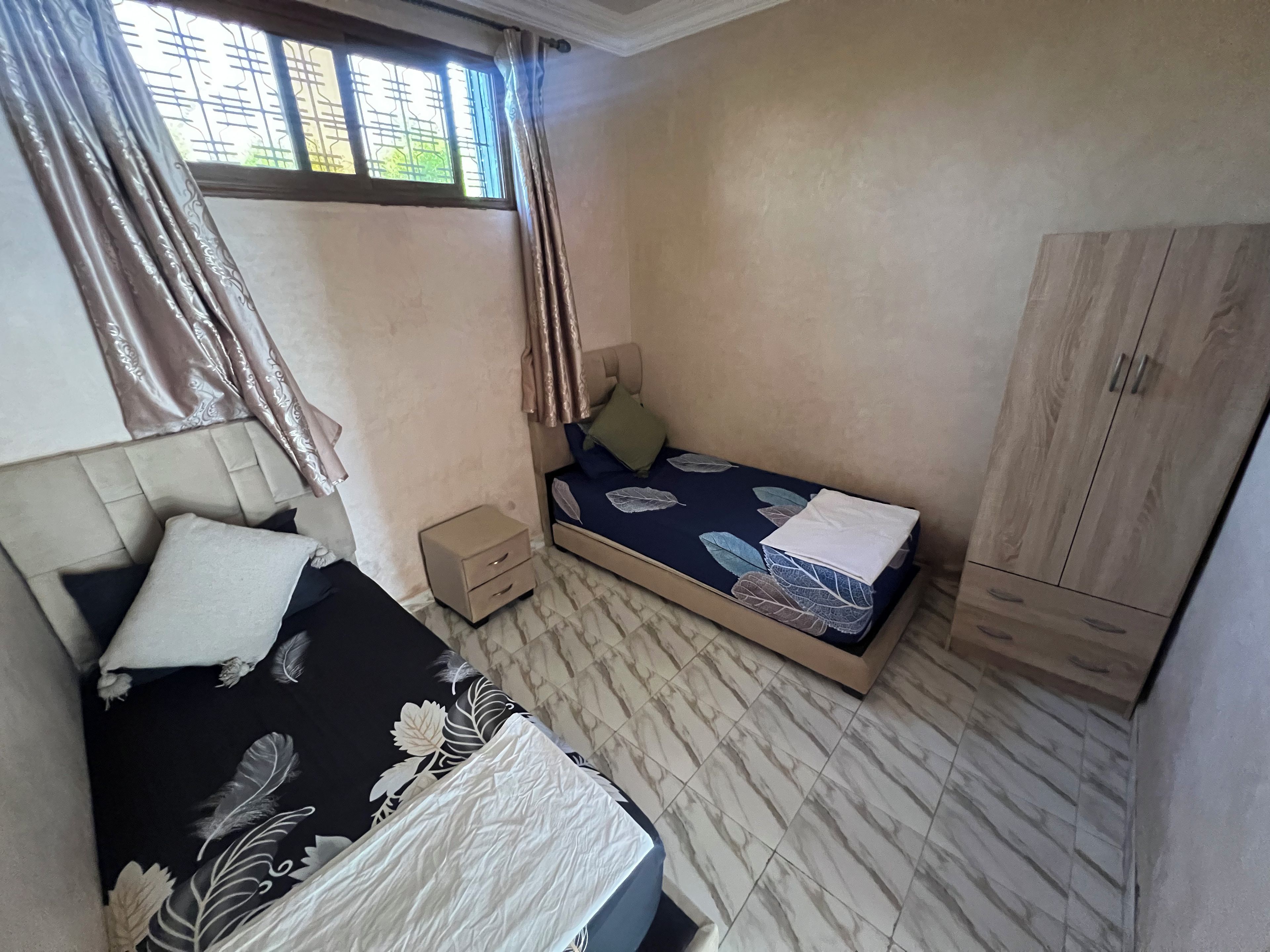 Een slaapkamer met een bed, nachtkastje, kledingkast en een raam met gordijnen.
