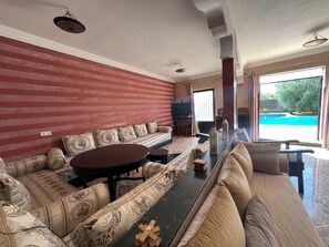 Amplio salón con un cómodo sofá, una mesa de comedor y vista a una piscina al aire libre.