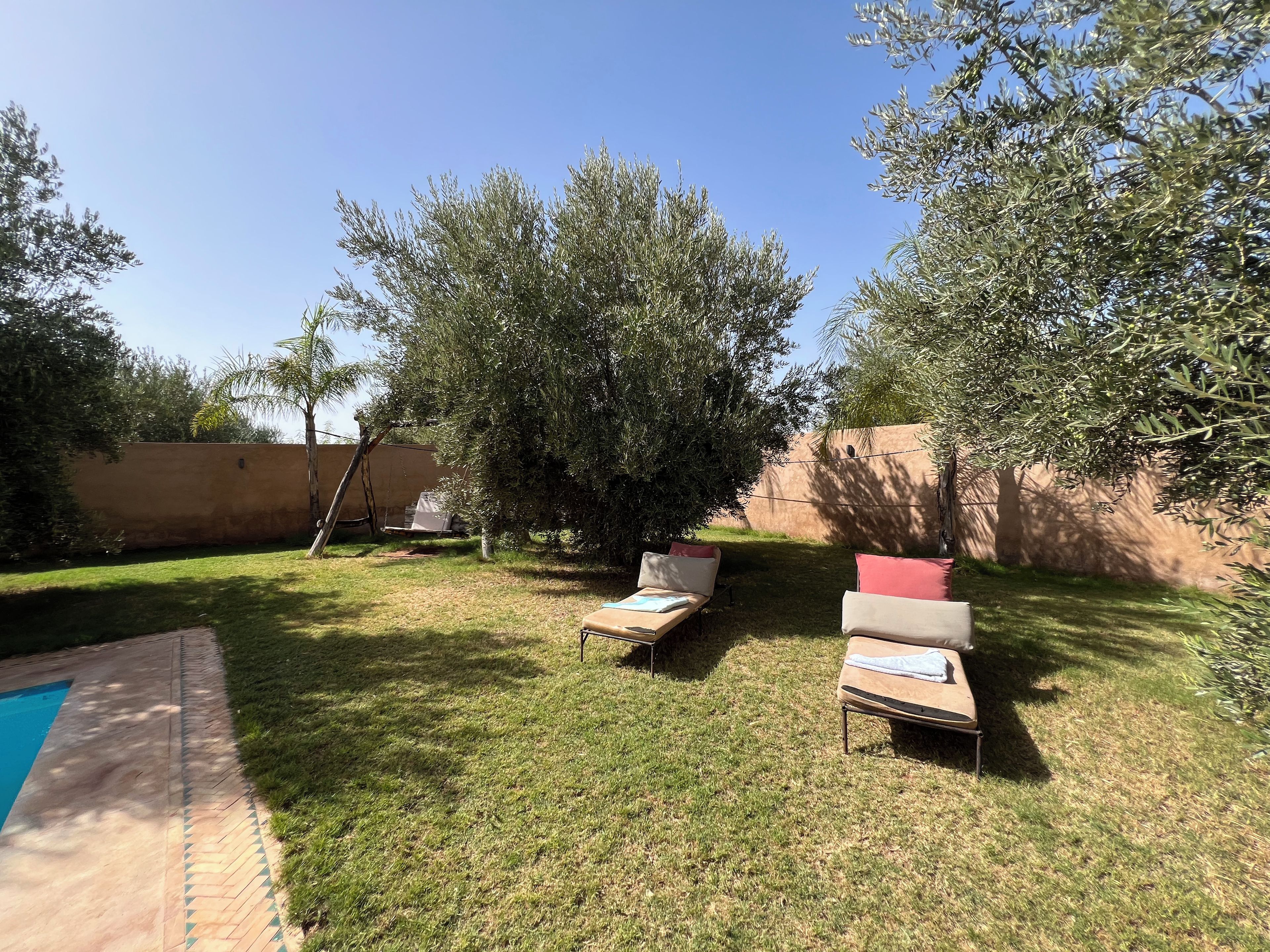 A backyard with a pool, two lounge chairs, and a pergola.