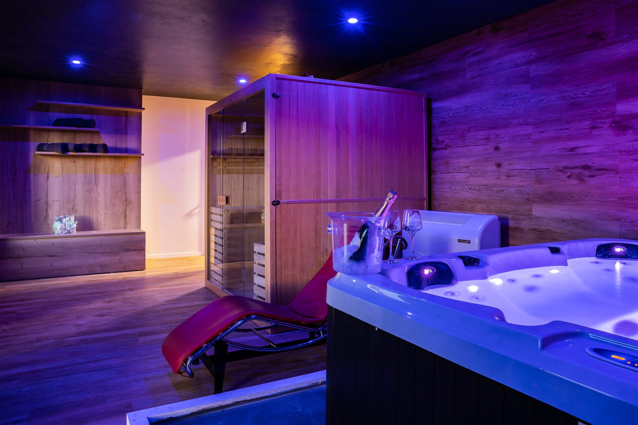A spa area with a wooden wall, a red chair, a hot tub, and a glass-enclosed sauna.