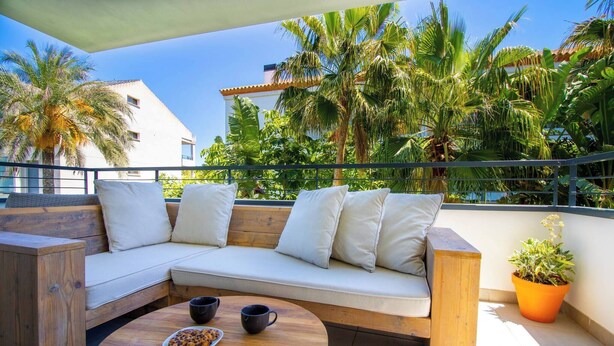 A wooden sectional sofa with white cushions, a round wooden table with two black cups and a plate of food, and a potted plant. - Samos Apartment (Badia de Xàbia)