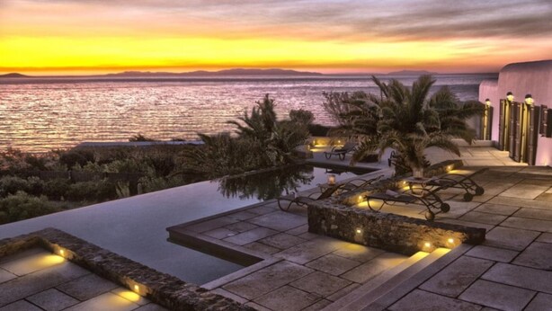 A rooftop infinity pool with stone borders and ambient lighting, overlooking a sunset over the sea. - Casa di Mare: Luxury and Breathtaking Views in Mykonos (Mykonos)