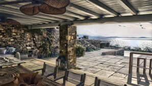 An outdoor patio with stone flooring, wooden furniture, and a stone wall. - Casa di Mare: Luxury and Breathtaking Views in Mykonos (Mykonos)