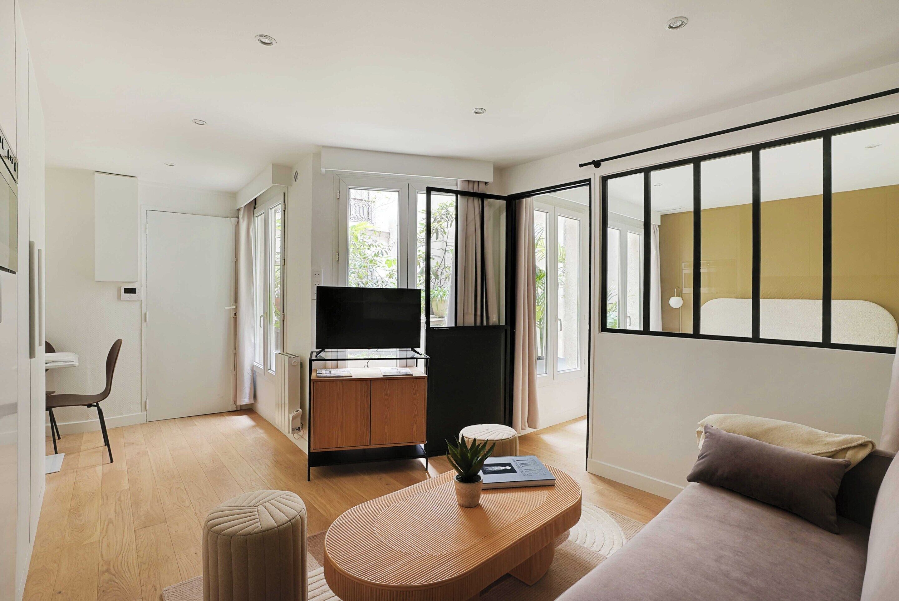 Una sala de estar moderna con un sofá, una mesa de centro, un televisor y una zona de cocina con un armario y un refrigerador.