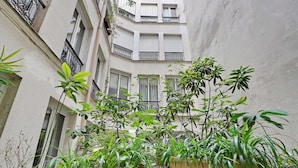 A narrow courtyard with multiple potted plants and a building with balconies.