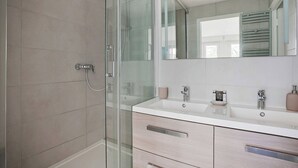 A modern bathroom with a glass shower enclosure, a double sink vanity, and a large mirror.