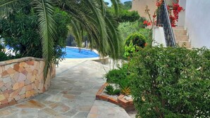 A stone pathway leading to a pool surrounded by lush greenery and a white building with a staircase. - Maxima Sunset KONTIKI 4 pers (Sainte-Maxime)