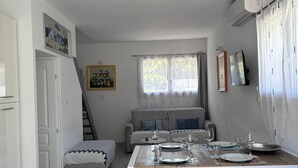 A living room with a dining table set for two, a sofa, a staircase, and a TV mounted on the wall. - Maxima Sunset KONTIKI 4 pers (Sainte-Maxime)