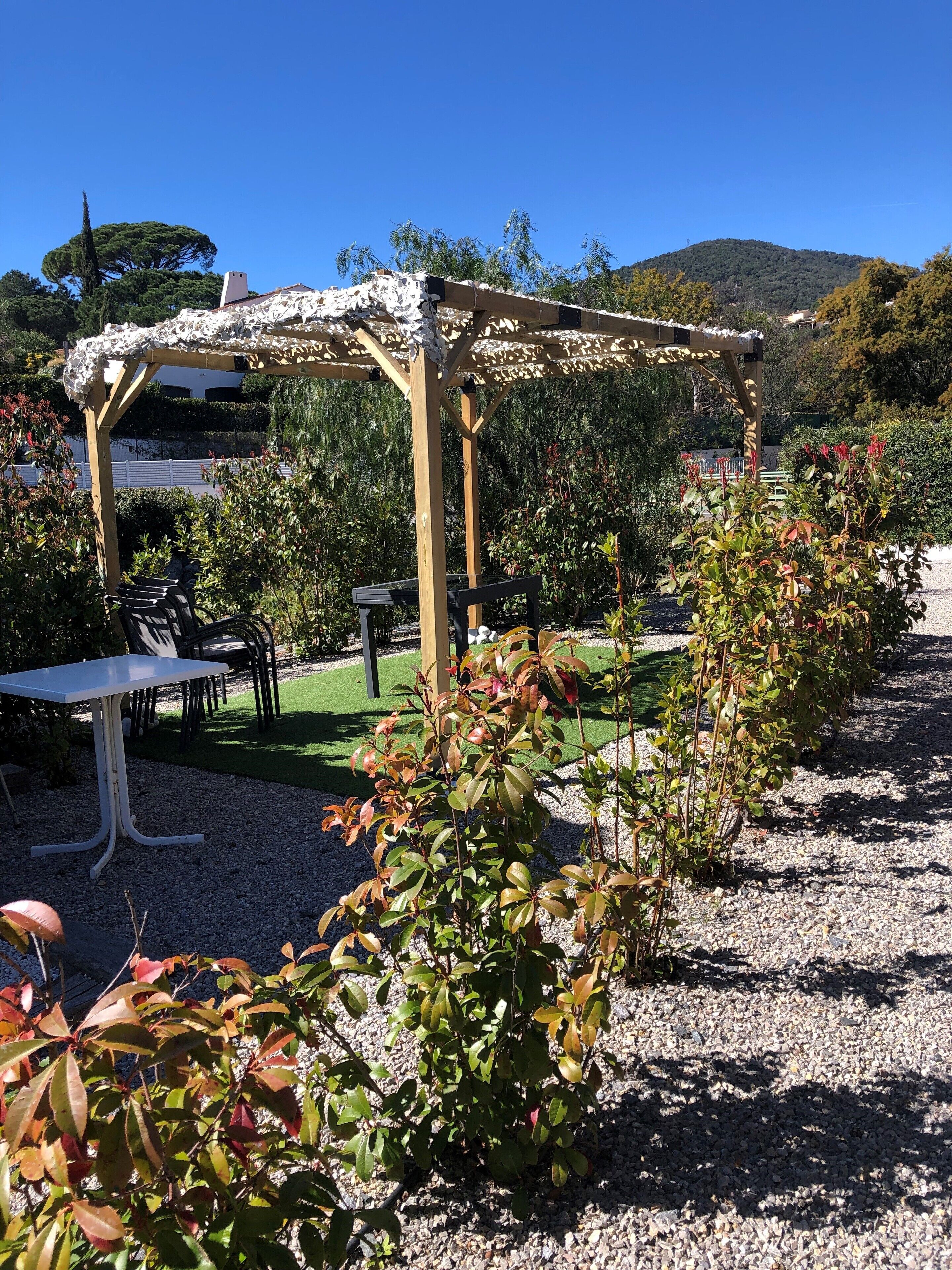 A garden with a pergola, seating area, and a gravel path.