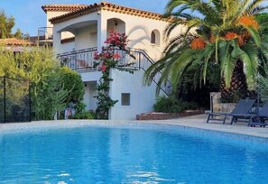 A swimming pool area with a white building, palm trees, and a balcony with pink flowers. - Maxima Sunset KONTIKI 4 pers (Sainte-Maxime)