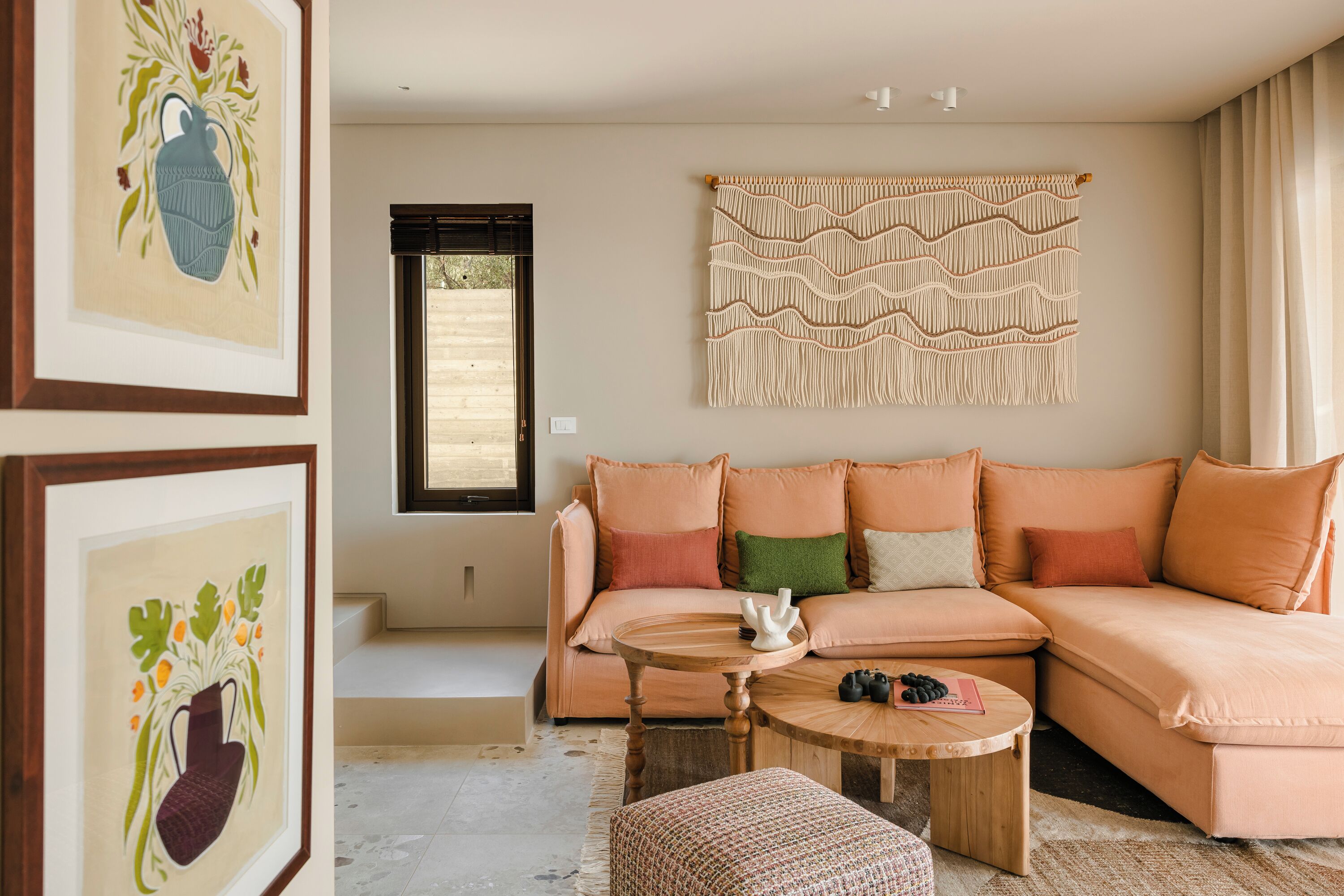 A cozy living room with a peach-colored sectional sofa, a round wooden coffee table, and a macramé wall hanging.