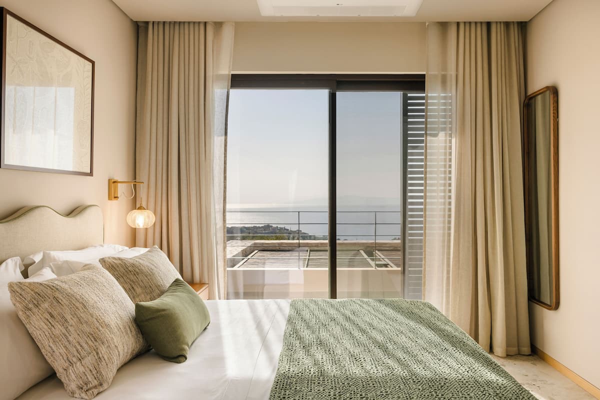 Ein Hotelzimmer mit Bett, Blick durch ein großes Fenster und einem Balkon.