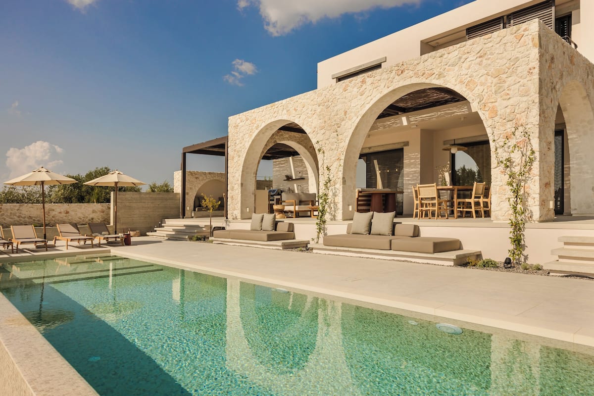 Ein moderner Poolbereich im Freien mit Steinarchitektur, Liegestühlen und einer Essgelegenheit.