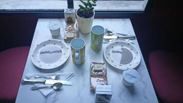 Ein gedeckter Tisch mit Tellern, Tassen, Besteck und verpackten Lebensmitteln.