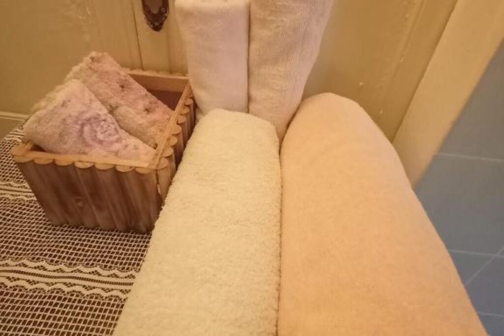 Une salle de bain avec une baignoire blanche, un tabouret en bois avec un coussin rose et un porte-serviettes blanc.