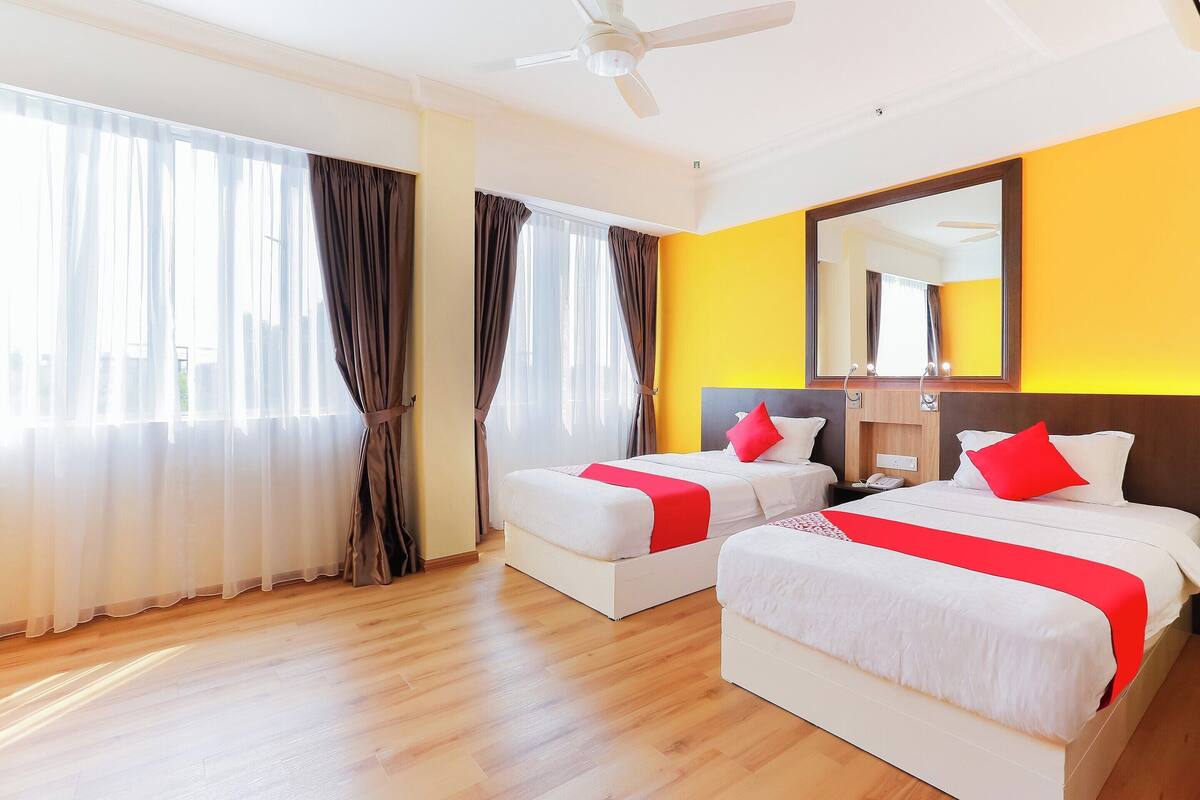 A hotel room with two beds, a ceiling fan, a large mirror, and a wooden floor.