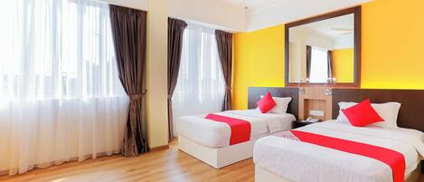 Habitación de hotel con dos camas, un ventilador de techo, un espejo grande y piso de madera.