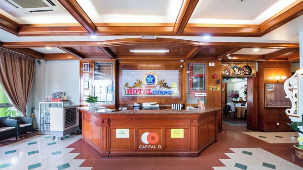 A hotel reception area with a wooden reception desk, a sign for Hotel Cowboy, and a counter with various items. - Collection O Hotel Super Cowboy (Malacca City)