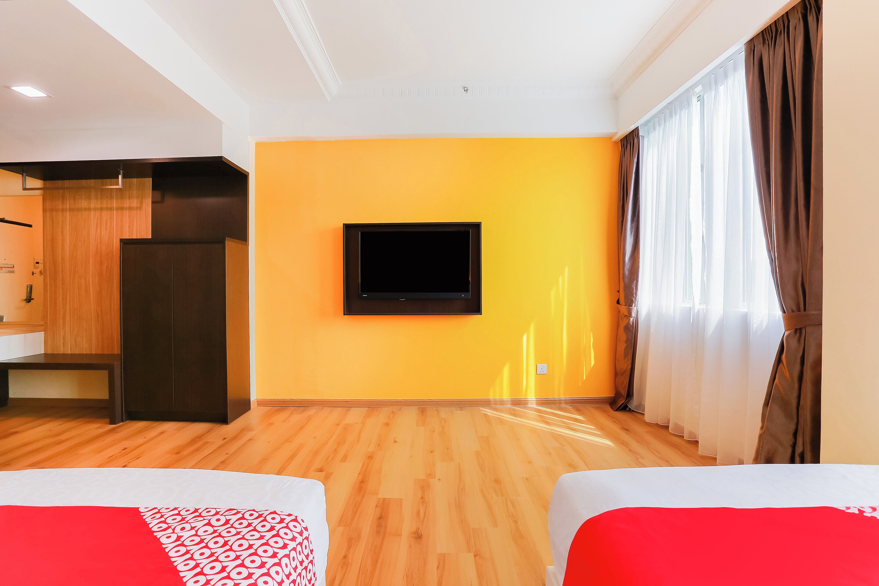 Une chambre d’hôtel avec un plancher en bois, un lit avec une literie rouge et blanche, un téléviseur fixé au mur et une fenêtre avec des rideaux.