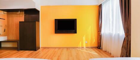 Une chambre d’hôtel avec un plancher en bois, un lit avec une literie rouge et blanche, un téléviseur fixé au mur et une fenêtre avec des rideaux.