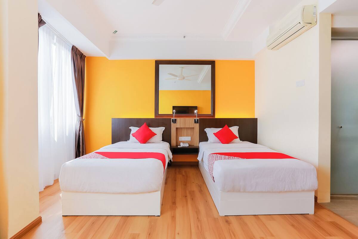 A hotel room with two single beds, a ceiling fan, an air conditioner, and a large mirror on the wall.